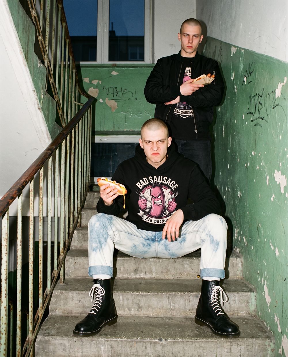 Model w czarnej bluzie Bad Sausage na schodach klatki